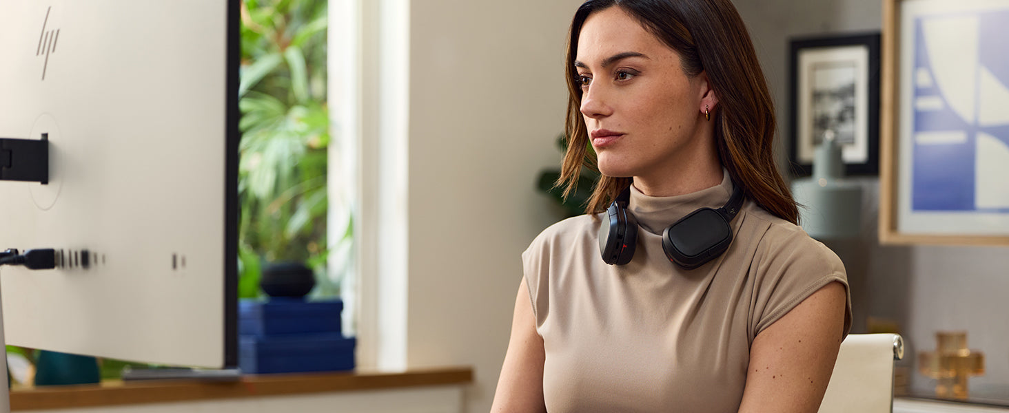 Person wearing HP Poly over-ear headset around neck in a modern home office setting