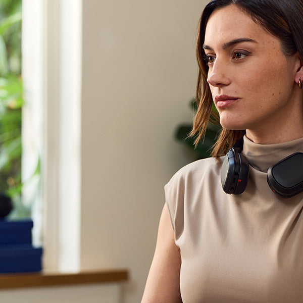 Person wearing HP Poly over-ear headset around neck in a modern home office setting