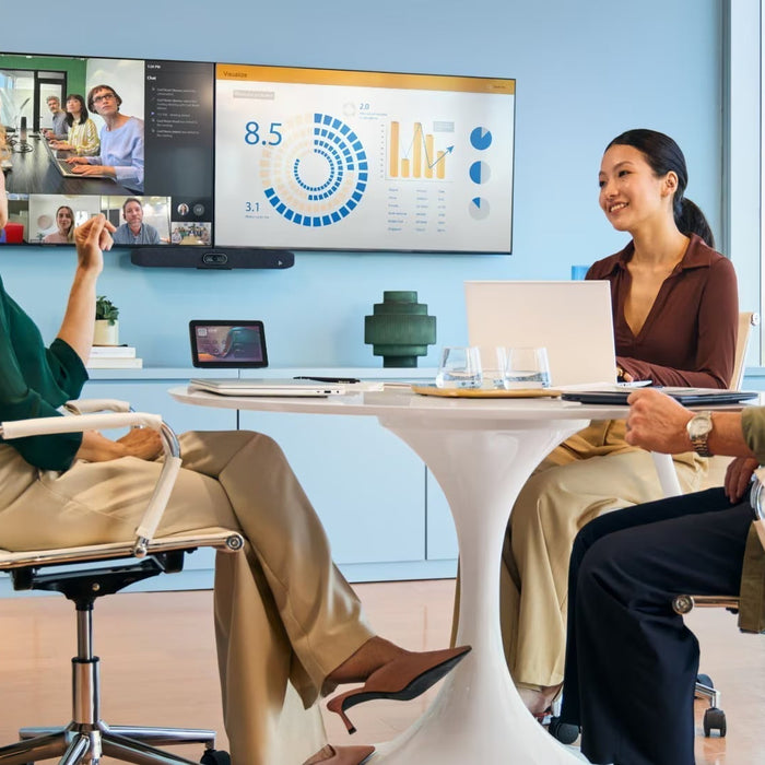 Small meeting room with three professionals using a Poly Studio USB video bar for a hybrid BYOD video conference on a large display