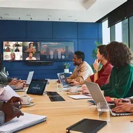 Team collaborating in a modern conference room using video conferencing technology for a hybrid meeting, showcasing a large display screen with remote participants